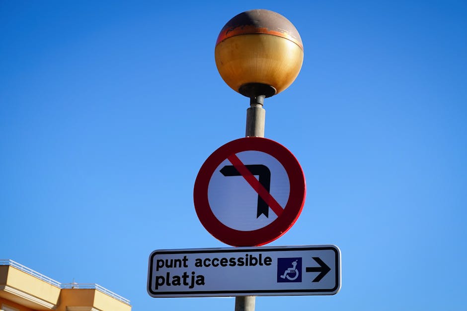 A street lamp with a rounded, weathered orange and black top stands against a clear blue sky. Below the lamp, there's a round no-turn sign with a black arrow crossed out in red. Beneath this, a rectan